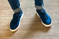 A person wears the Kizik Men's Prague 2 Sneakers on a jute rug