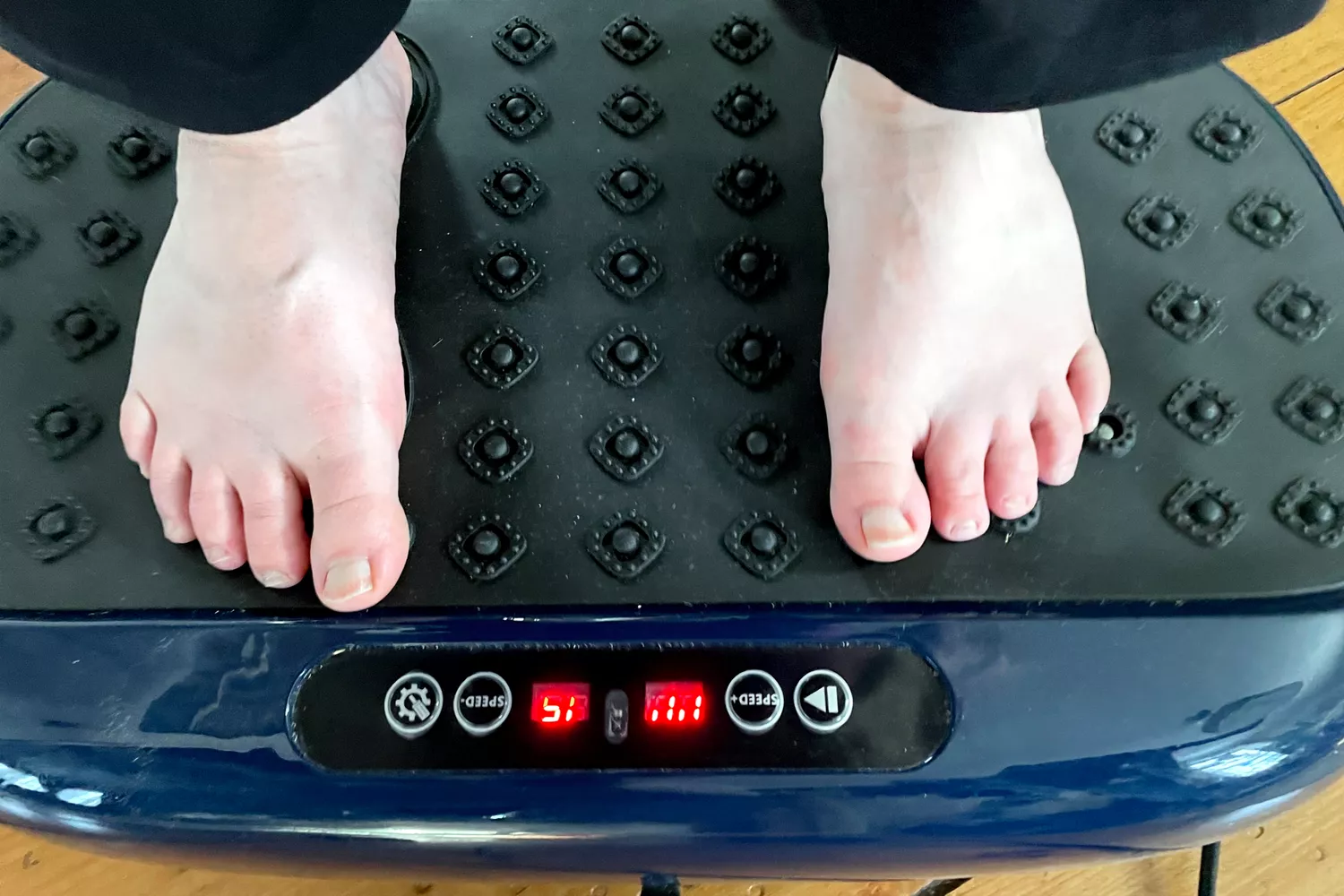 A person stands barefoot on the LifePro HexaPlate Lite Vibration Plate