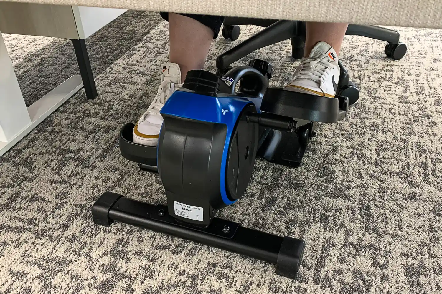 A person pedals the LifePro FlexStride Plus while sitting at a desk