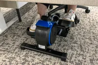 A person pedals the LifePro FlexStride Plus while sitting at a desk