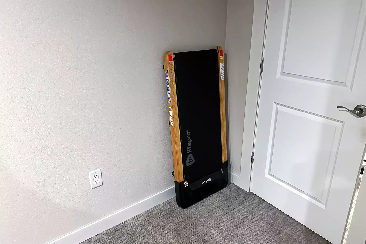 The LifePro TimberTrek Treadmill leaning on a wall by a door