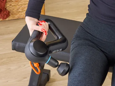 Person holding a massage gun near their leg on a bench.
