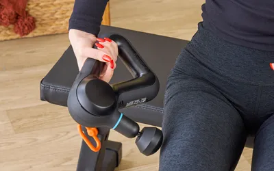 Person holding a massage gun near their leg on a bench.