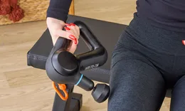 Person holding a massage gun near their leg on a bench.