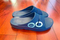 A pair of OOFOS OOahh Slide Sandals on a wooden floor