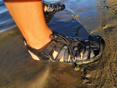 A close up of a person wearing the KEEN Men's H2 Water Sandals on a beach