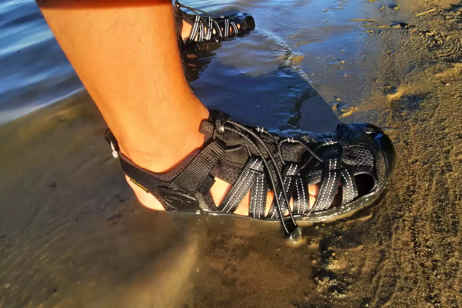A close up of a person wearing the KEEN Men's H2 Water Sandals on a beach