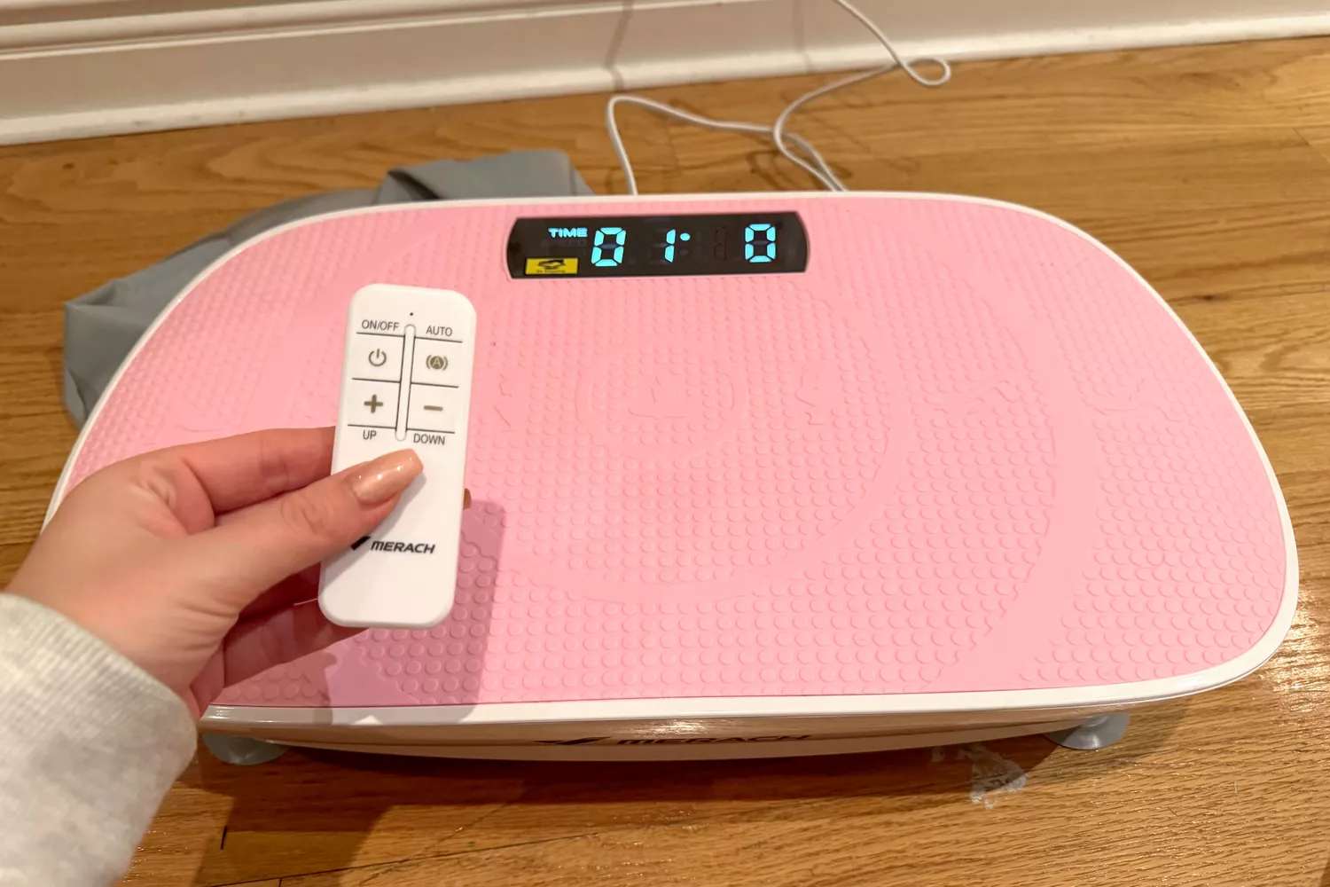 A person controls the Merach Whole Body Vibration Plate with a remote control