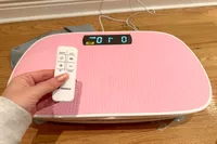 A person controls the Merach Whole Body Vibration Plate with a remote control