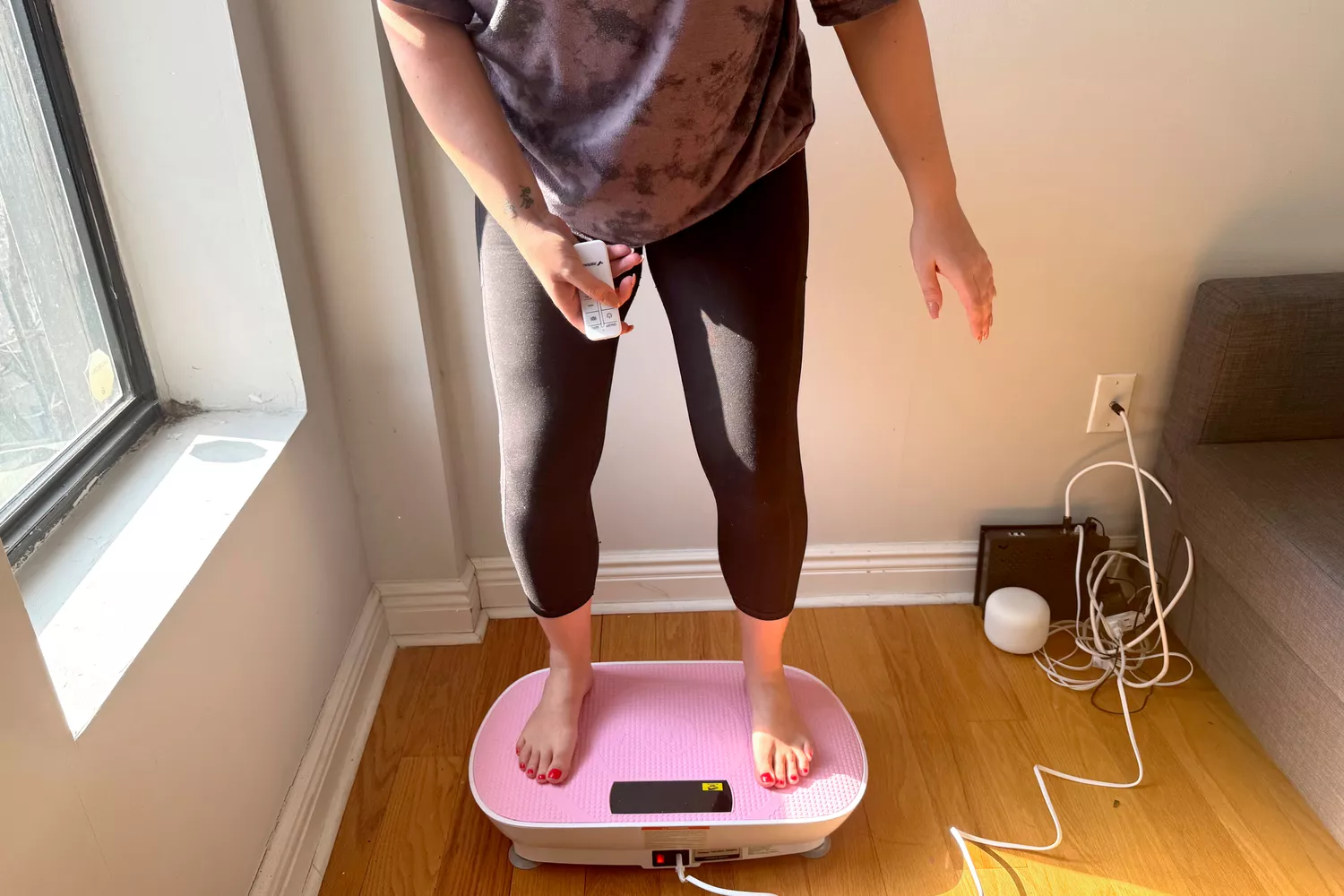A person stands on the Merach Whole Body Vibration Plate while using the remote control