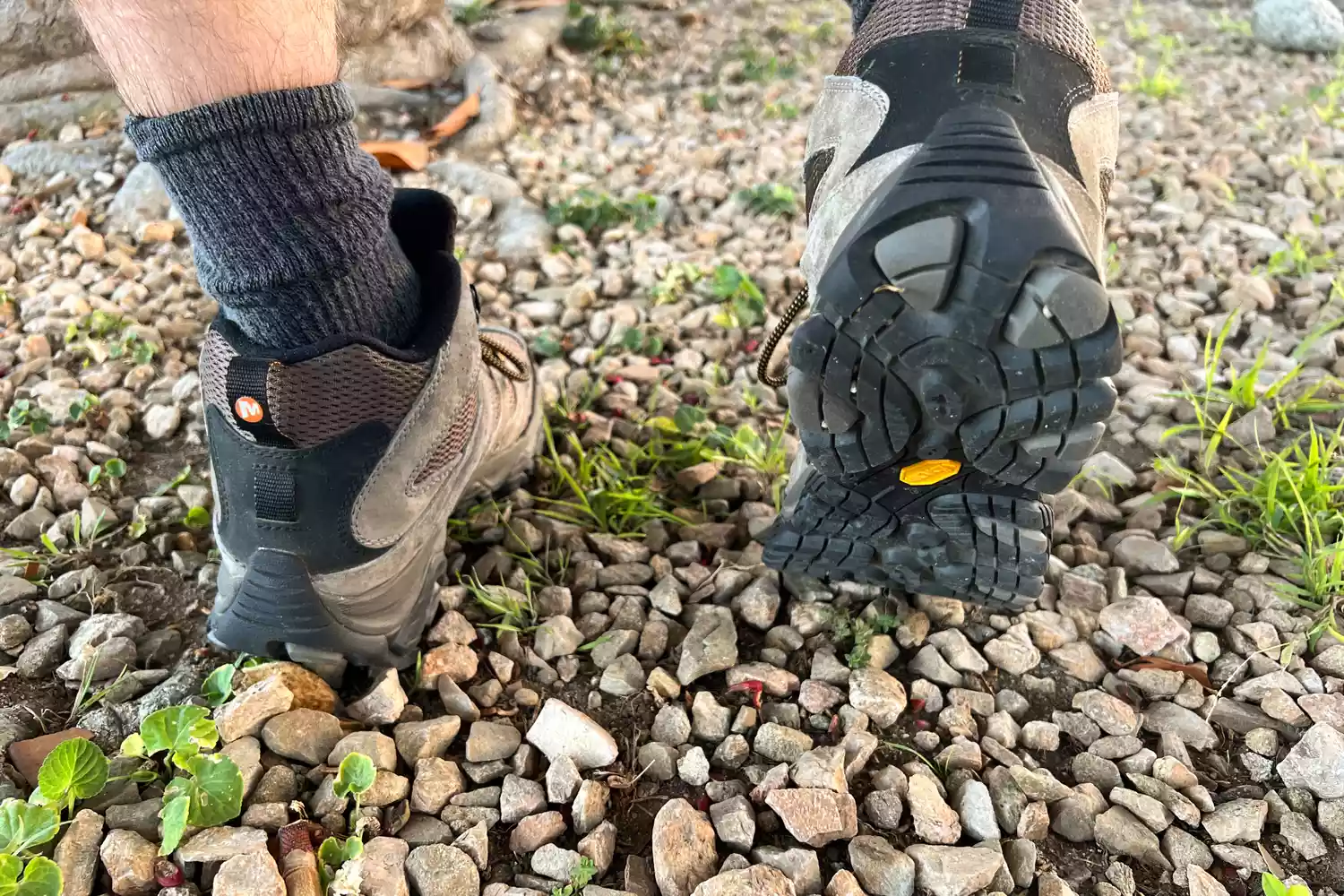 Feet wearing Merrell Men's Moab 3 Mid Hiking Boot with one heel lifted