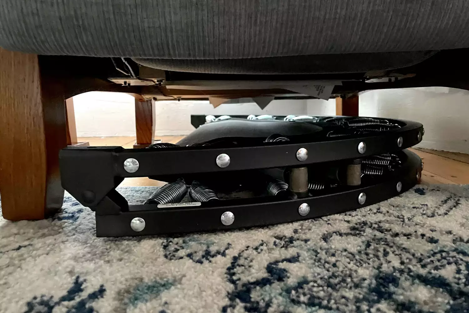 The Needak Soft-Bounce Folding Rebounder folded and placed under a chair for storage