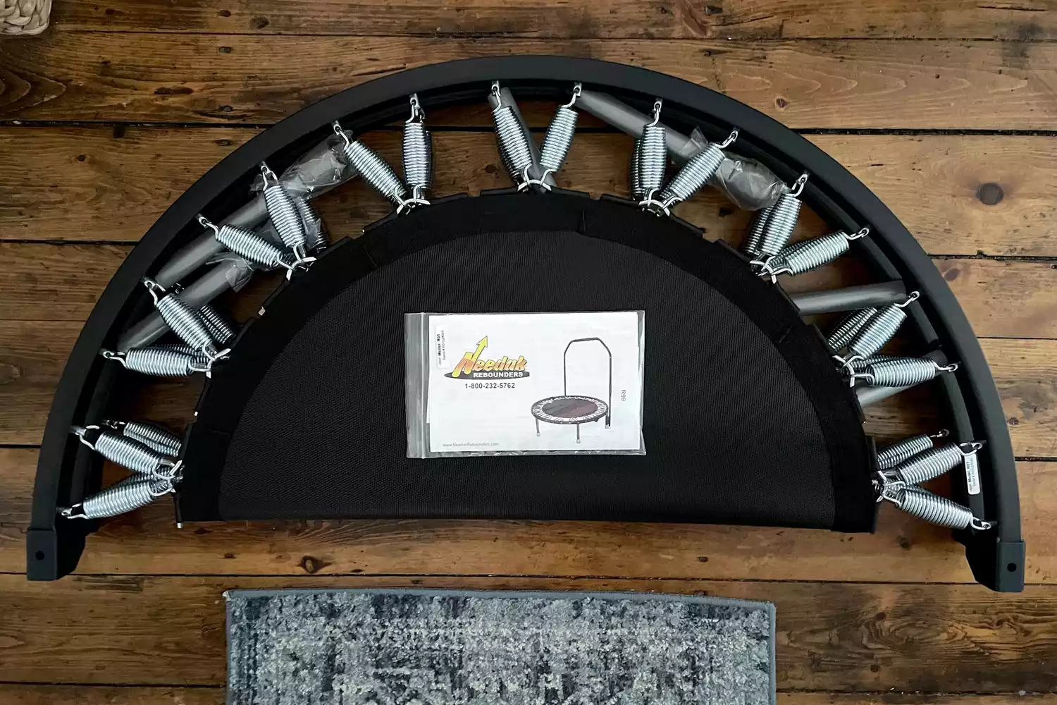 The Needak Soft-Bounce Folding Rebounder folded in half with the user manual on top