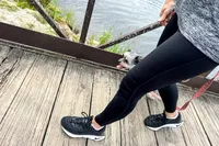 A person walking on a wooden bridge with a small dog on a leash wearing the Nike Motiva Women's Walking Shoes