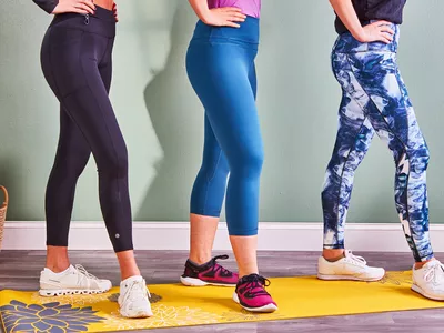 Three people wearing leggings and sneakers posing on a yellow yoga mat with their hands on their hips