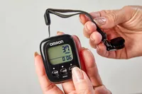 A person presses a button on the Omron Walking Style IV Pedometer