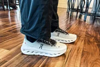 A person stands inside while wearing the On Men's Cloudtilt Walking Shoes