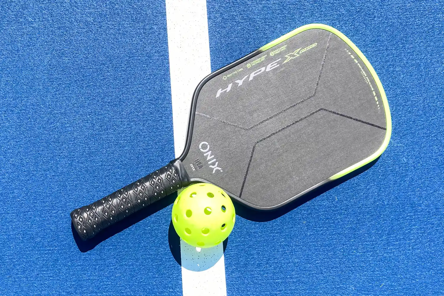 The Onix Hype X Pro Raw Carbon Pickleball Paddle next to a pickleball