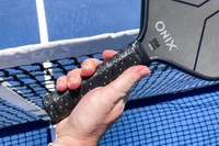 A person holds the Onix Hype X Pro Raw Carbon Pickleball Paddle by the handle