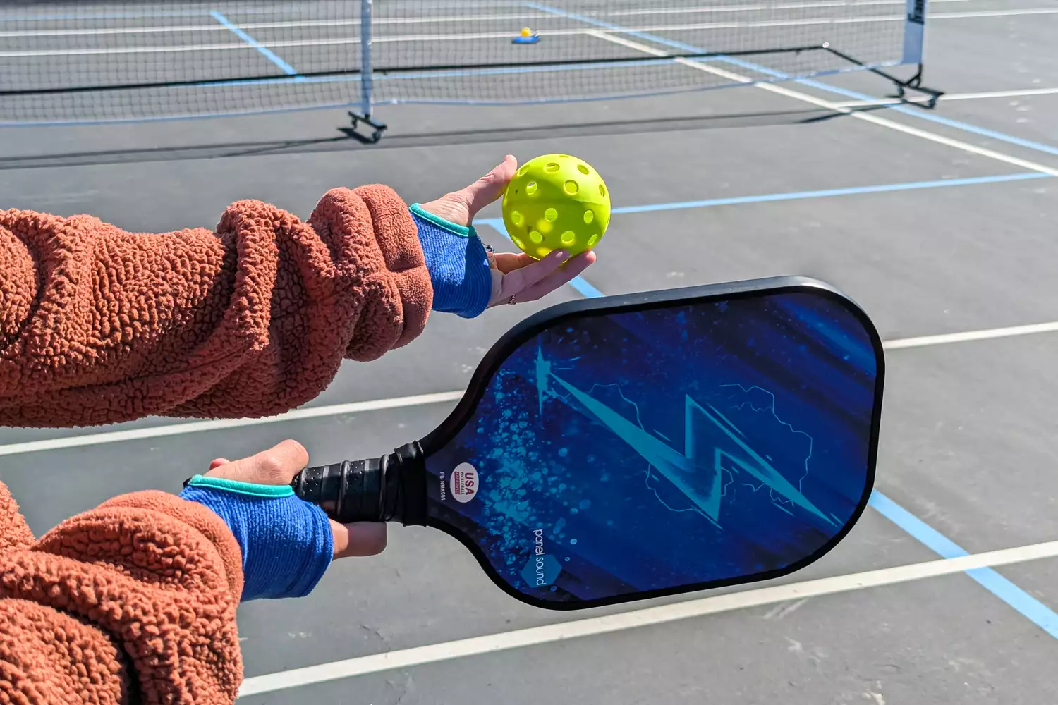 A person holding a ball and a Panel Sound Pickleball Paddle