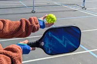 A person holding a ball and a Panel Sound Pickleball Paddle