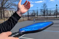 A hand holding the Panel Sound Pickleball Paddle in serve preparation position