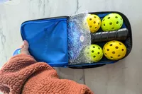A hand opening a carrying case for the Panel Sound Pickleball Paddles Set of 2 and balls