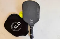 The Six Zero 16mm Double Black Diamond Control Pickleball Paddle with cover next to a pickleball