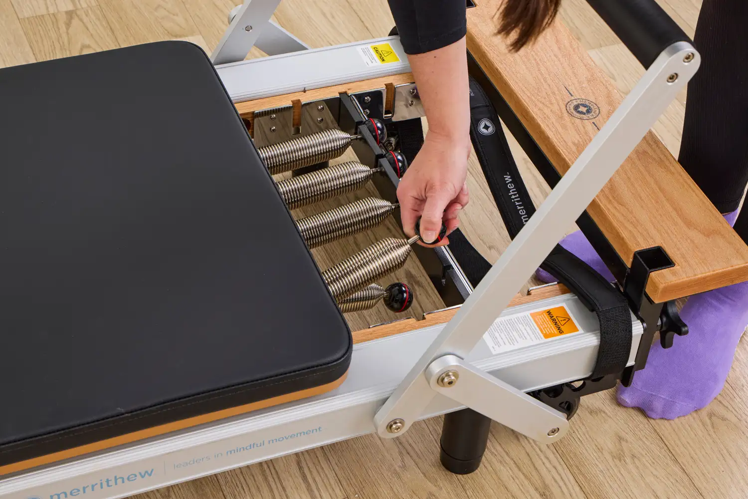 A person adjusts the springs on the Merrithew At Home SPX Reformer Bundle