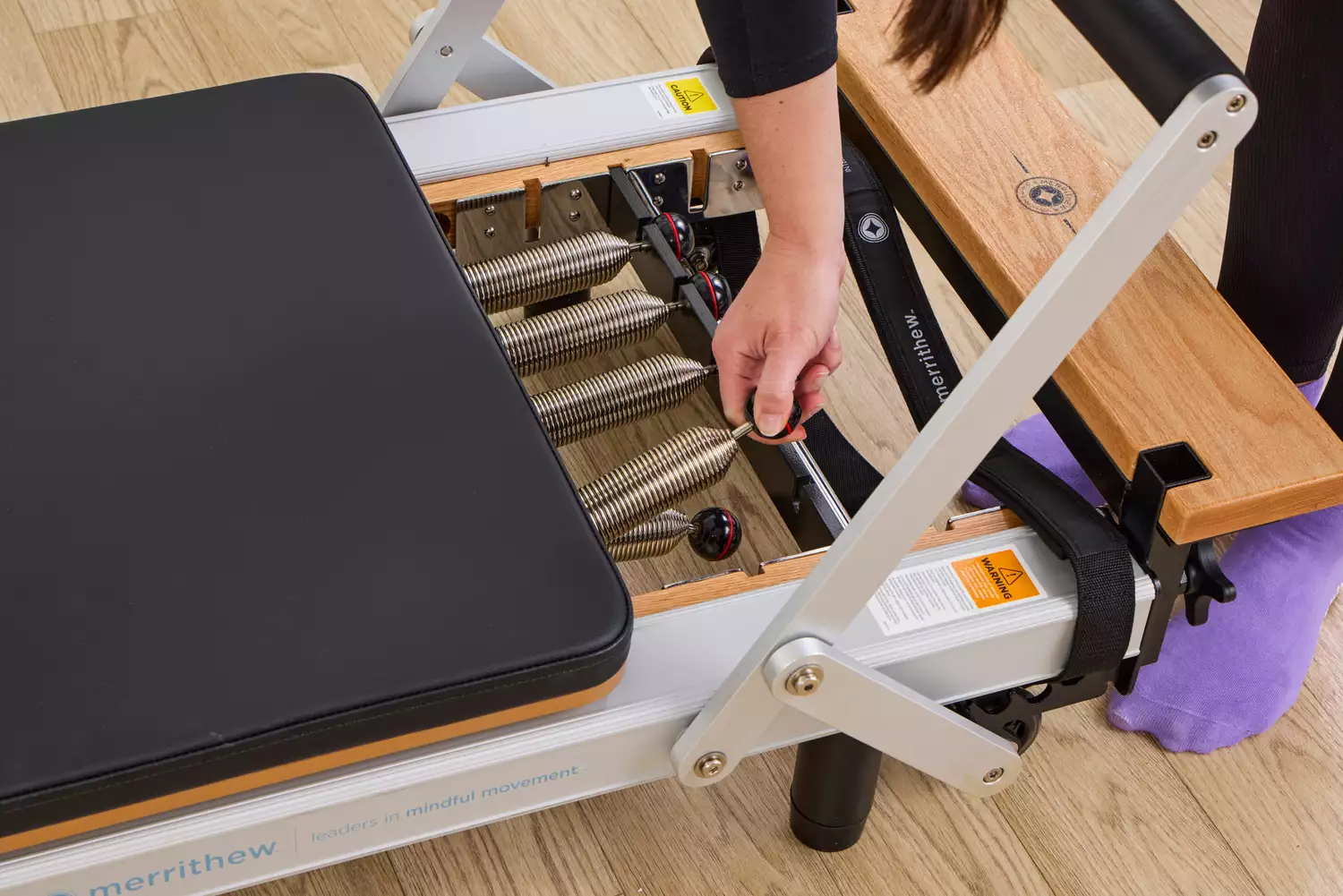 A person adjusts the springs on the Merrithew At Home SPX Reformer Bundle