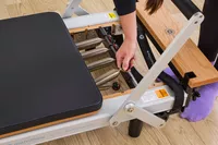 A person adjusts the springs on the Merrithew At Home SPX Reformer Bundle