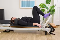 A person exercises using the Merrithew At Home SPX Reformer Bundle