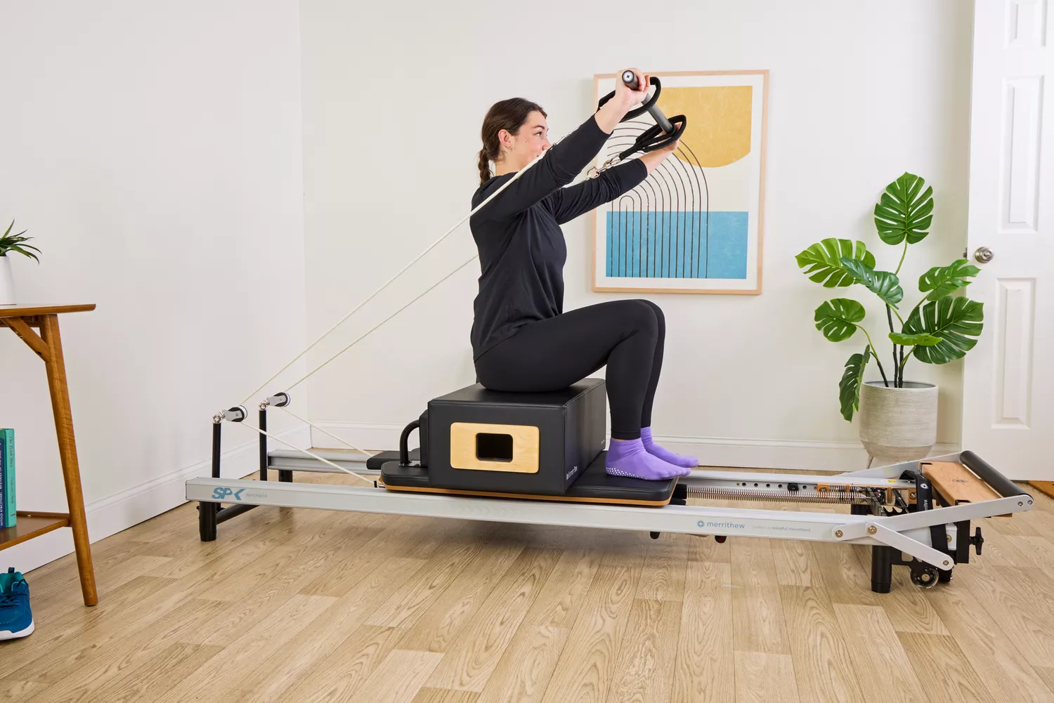 A person exercises while sitting on the Merrithew At Home SPX Reformer Bundle
