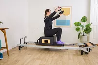 A person exercises while sitting on the Merrithew At Home SPX Reformer Bundle