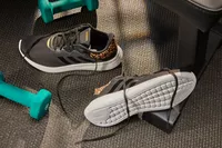 Adidas Women's Cloudfoam Qt Racer Running Shoe displayed on a black floor next to dumbbells