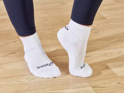 Feet wearing Asics Cushion Quarter Running Socks on a wood floor with one heel lifted