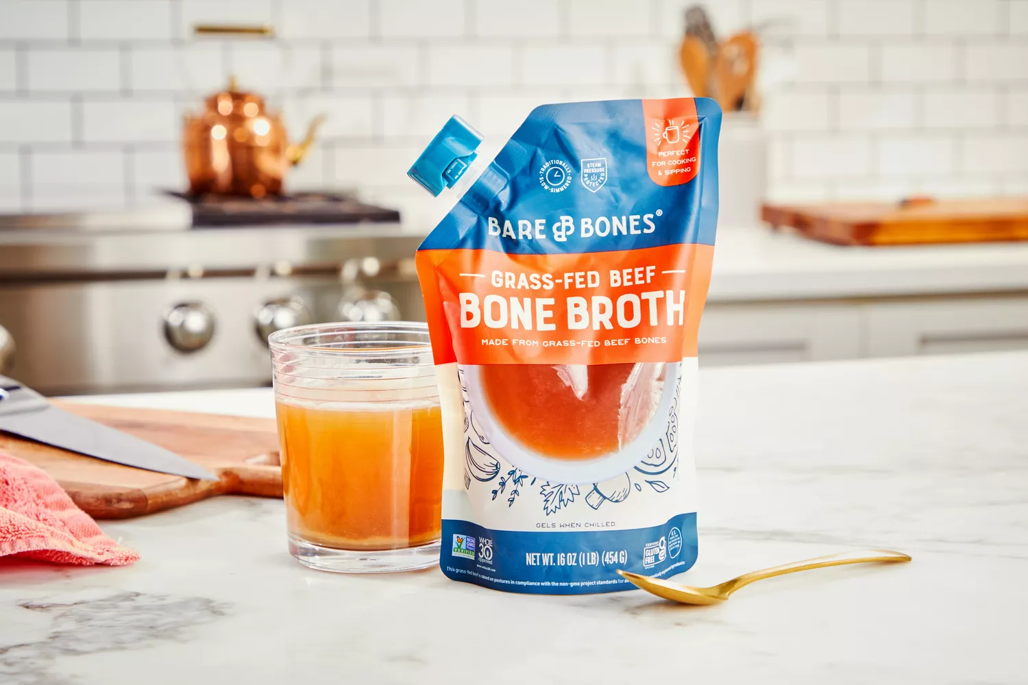 A pouch of Bare Bones Grass-Fed Beef Organic Bone Broth next to glass of broth on countertop
