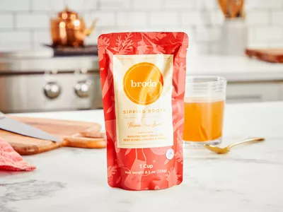 A packet of Brodo Hearth Bone Broth displayed on counter with glass of broth