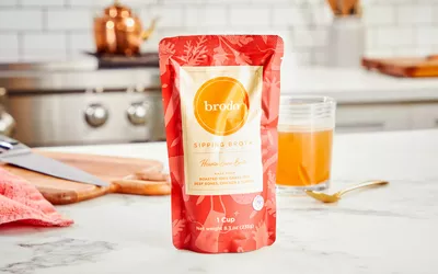 A packet of Brodo Hearth Bone Broth displayed on counter with glass of broth
