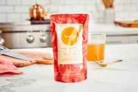 A packet of Brodo Hearth Bone Broth displayed on counter with glass of broth