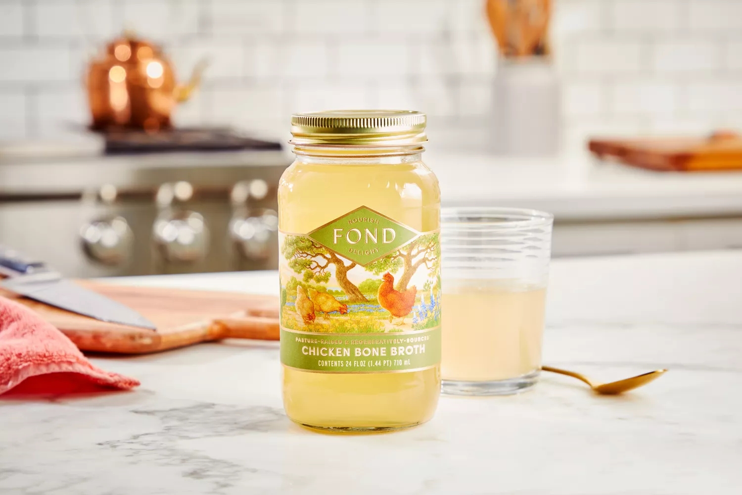 A jar of FOND Certified Organic Chicken Bone Broth on counter with glass in background