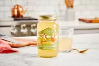 A jar of FOND Certified Organic Chicken Bone Broth on counter with glass in background
