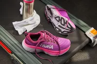 Pink Hoka Women's Bondi 8 Running Shoes displayed on a treadmill with a towel and water bottle