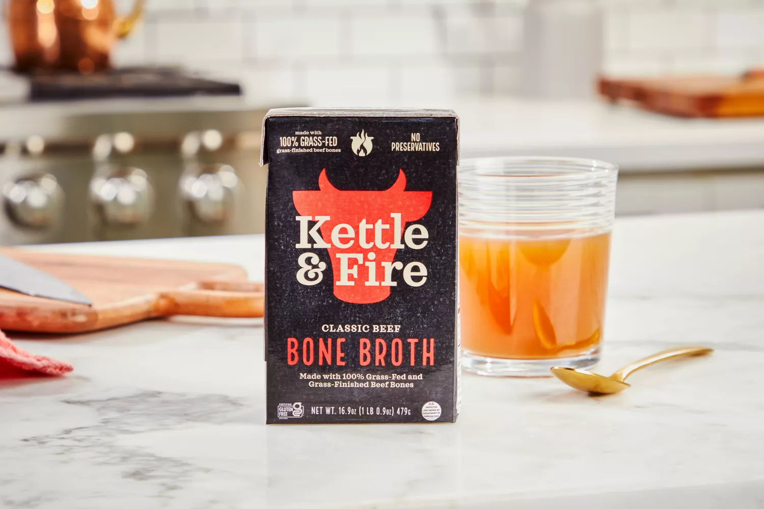 A box of Kettle & Fire Bone Broth and glass of broth on kitchen countertop