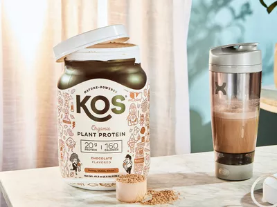 KOS Vegan Superfood Protein Powder bottle next to a scoop and shaker