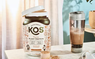 KOS Vegan Superfood Protein Powder bottle next to a scoop and shaker