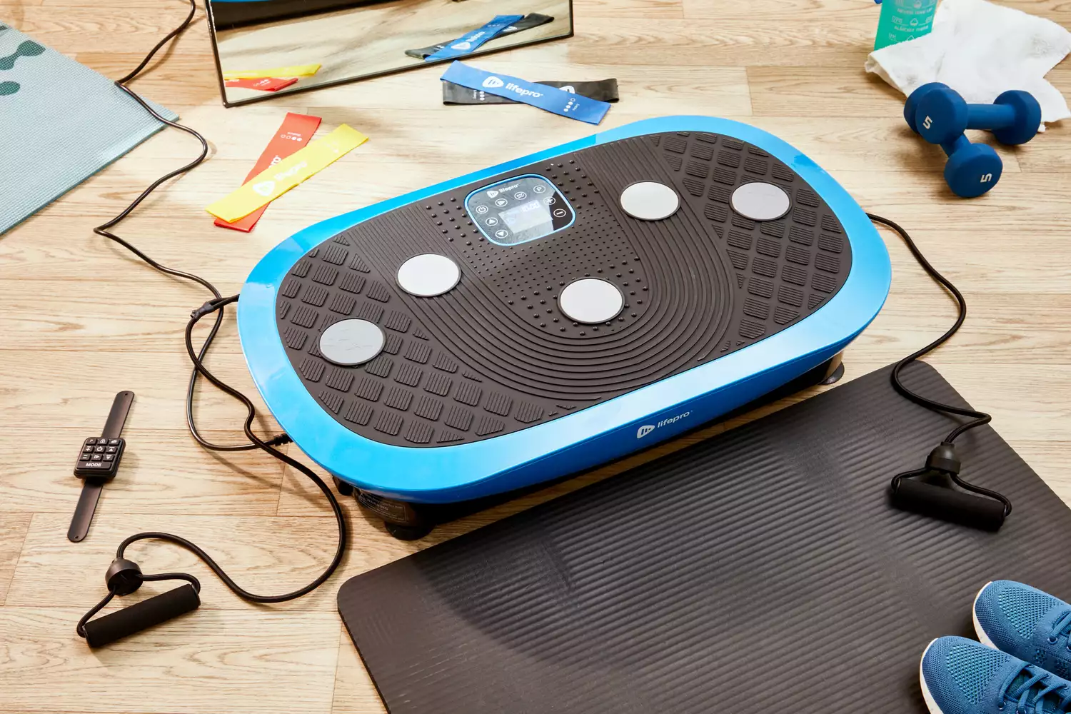 The LifePro Rumblex Plus 4D Vibration Plate Exercise Machine on the floor near accessories