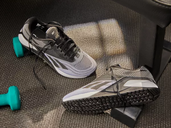 A pair of Reebok Men's Nano X2 Cross Trainers on the floor next to weights and a workout bench.