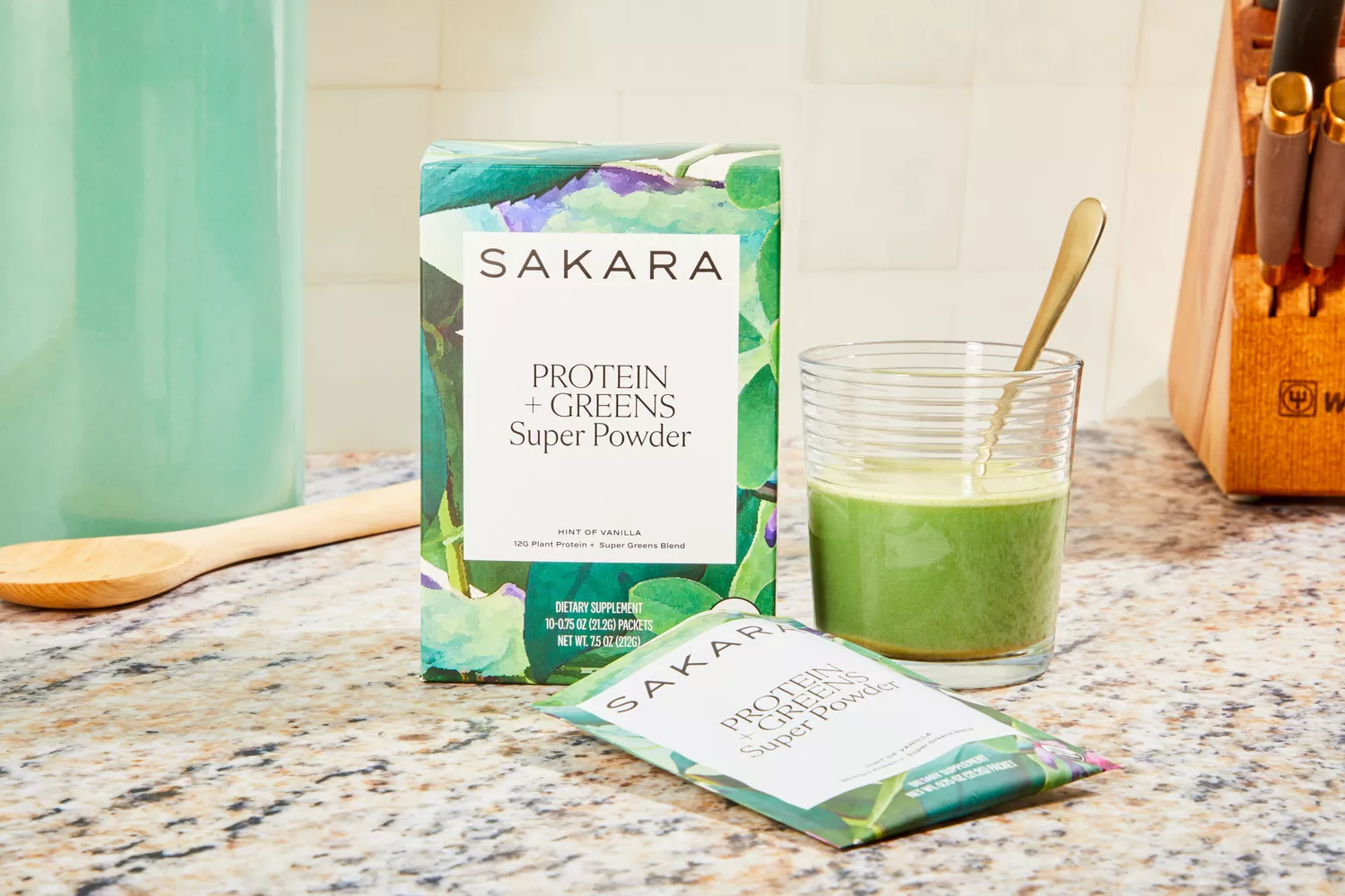 Sakara Organic Protein + Greens Super Powder displayed mixed with water in a glass with its packaging on a marble counter