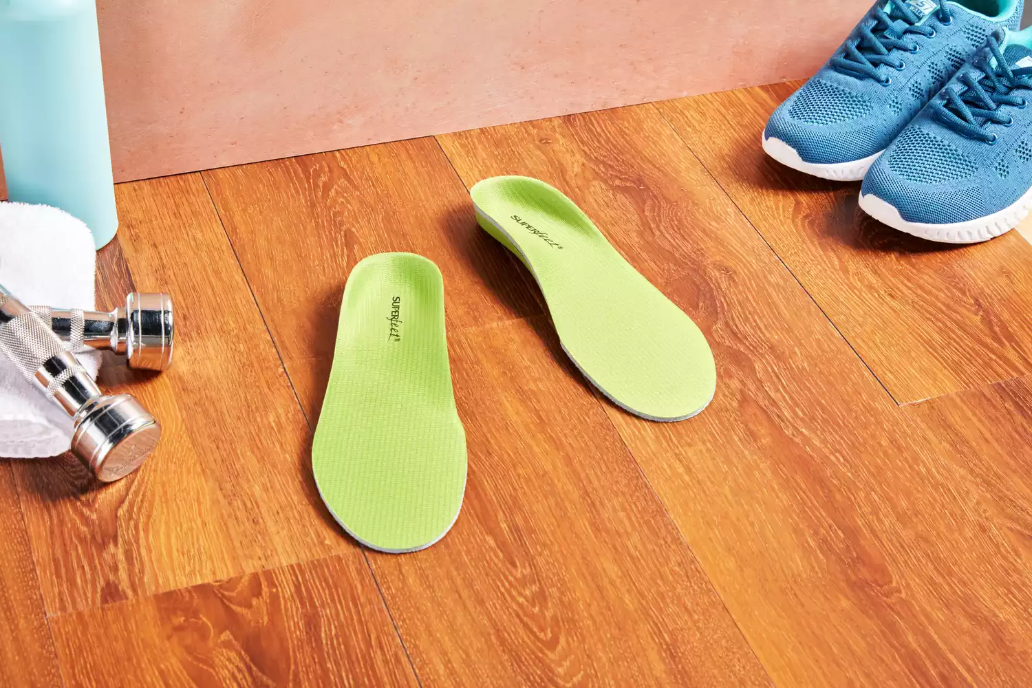 Superfeet Green Insoles displayed on wooden floor next to shoes